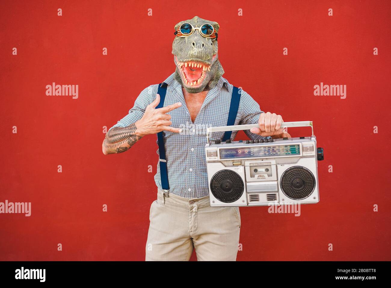 Verrückter Senior tanzt Rockmusik mit t-rex-maske - Tattoo trendiger Kerl mit Spaß Musik mit Boombox-Stereo - Absurder und lustiger Trend-Con Stockfoto