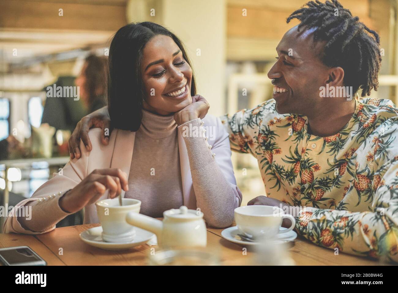 Fröhliches schwarzes Paar trinkt Kaffee im Vintage-Bar-Restaurant - Trendige junge Leute, die Spaß haben zu sprechen und zum Frühstück zu lachen - Liebe und Lachen Stockfoto