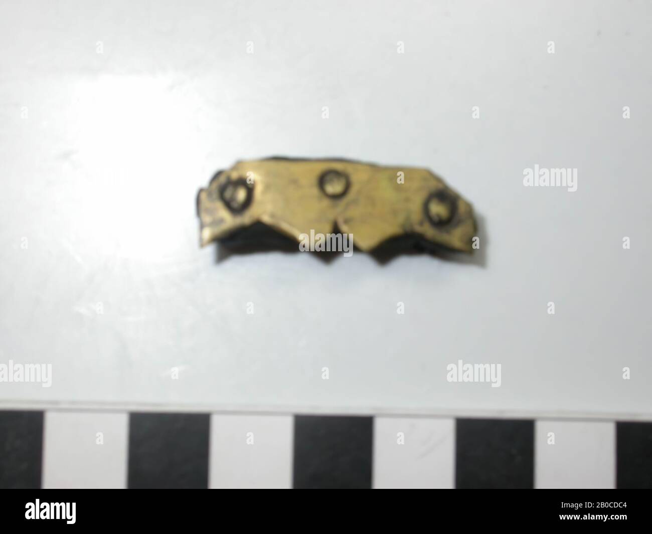 Goldfarbene Armaturen (Kupferlegierung), in rechteckiger Form. Die beiden Ecken auf einer Langseite sind abgeschnitten, die andere Langseite ist gezähnt und hat an den Außenseiten zwei Dreiecke in der Mitte und ein halbes Dreieck. Die Kanten der Dreiecke sind nach unten gebogen. Der Batter wird mit drei goldfarbenen Nieten, von denen zwei übrig sind, an verschiedenen Lederschichten befestigt. So gibt es Freiräume zwischen Schlagwerk und erster Lederschicht und zwischen zweiter Lederschicht und Ende der Ziernägel. Das Leder ist so breit wie der Teig, die Länge beträgt 3,1 - 3. Stockfoto