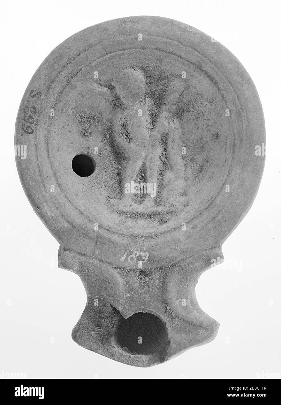 Eine Öllampe aus hellrotem Steingut mit rundem Gehäuse. Der konkave Spiegel ist von eingelassenen konzentrischen Kreisen umgeben und mit einem stehenden Eros mit einer Fackel verziert. Das kleine Füllloch befindet sich links von der Abbildung. Der kurze, breite Ausguss ist mit Voluten, Öllampe, Steingut, Terrakotta, 2,8 x 9,6 x 7 cm, AD aus dem 1. Jahrhundert gerahmt. 1-100, Asien Stockfoto