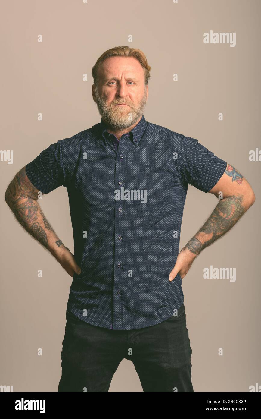 Studio shot reifer bärtiger Mann mit hand Tattoos auf den Hüften in grauer Hintergrund posiert Stockfoto