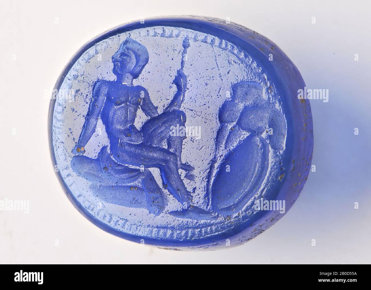 VZ: Der Mann sitzt auf einem Felsen (?), Wo er sein linkes Bein gehoben hat, er hat den Kopf nach links gedreht, mit der rechten Hand lehnt er sich an den Felsen und mit der linken Hand hat er einen Stab, Gegenüber dem Mann befindet sich ein Felsen, an dem sich ein Schild lehnt, die Szene ist von einem Band kleiner Quadrate umgeben., GEM, intaglio, unbekannt, Farbe: Dunkelblau, Form: Oval, Verarbeitung: Kante vorne nach hinten geschnitten, 11 x 10 x 2 mm Stockfoto