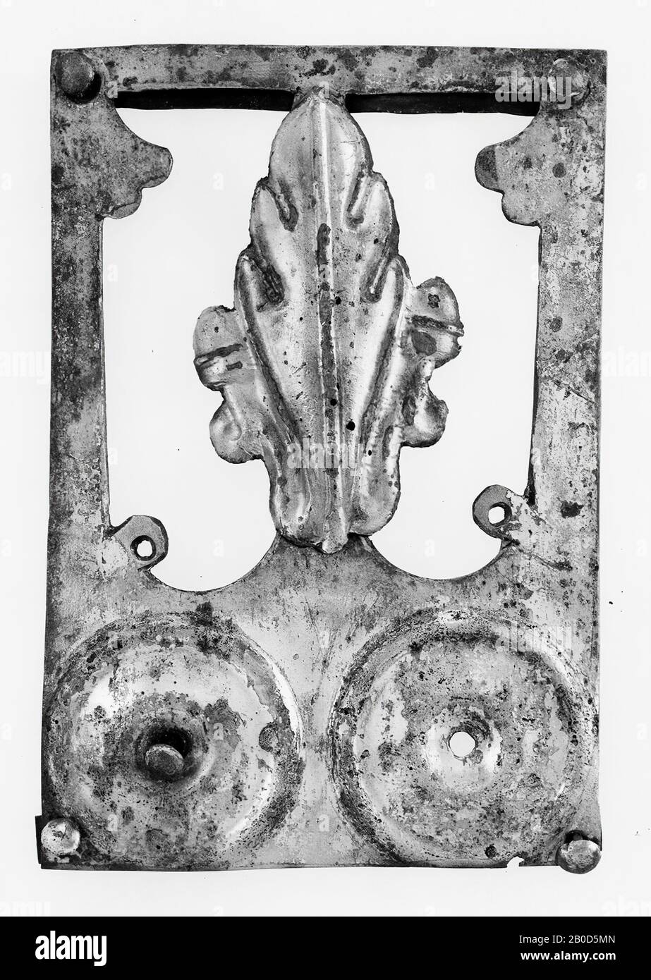 Rechteckige versilberte Bronzeplatte. Oben befinden sich zwei runde Verzierungen (mit einem konkaven Mittelfeld, das ein Lochfeld umschließt), um die ein Rand, zuerst konvex als konkave, geschlossen von einem dicken Grat) herausgetrieben wird. Darunter befindet sich ein großes dekoratives Motiv. Zwei längliche Bogenfenster sind nebeneinander ausgeschnitten. An den Außenseiten der Fenster verbleiben ein Kreis (mit einem Loch in der Mitte) und unten ein fächerförmiges Muster in Bronze. Auf dem dünnen, dazwischen liegenden Stil, der die beiden Fenster voneinander trennt, ist eine Zierde verlötet: Ein konvexes Eichenblatt mit einer Akorn auf beiden Seiten. Hinten sind sie kurz Stockfoto