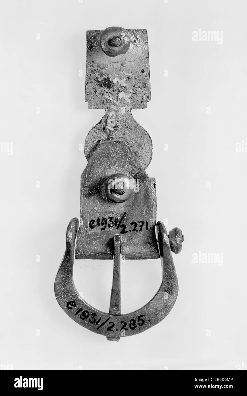 Langplatte aus versilberter Bronze. Es hat zwei Kerbpaare auf beiden Seiten, wodurch es rechteckig, mehr oder weniger oval und dann wieder rechteckig in Form ist. Im unteren rechteckigen Teil befinden sich auch 1 Kerbpaar. Dekoriert mit Stielen, die in Blättern enden. Auf der Rückseite befindet sich an beiden Enden eine Leiste mit einem Ring. An der oberen Leiste ist eine Schnalle befestigt. Diese Schnalle besteht aus einem doppelt gefalteten Stück Bronze, dessen Enden schräg abgeschnitten sind. Auf dem Falz wurde eine Kerbe hergestellt, während ein Bronzestab durch den Falz geschnitten wurde. Dies ist der Stift der Schnalle in der Kerbe. Wsch schloss um Stockfoto