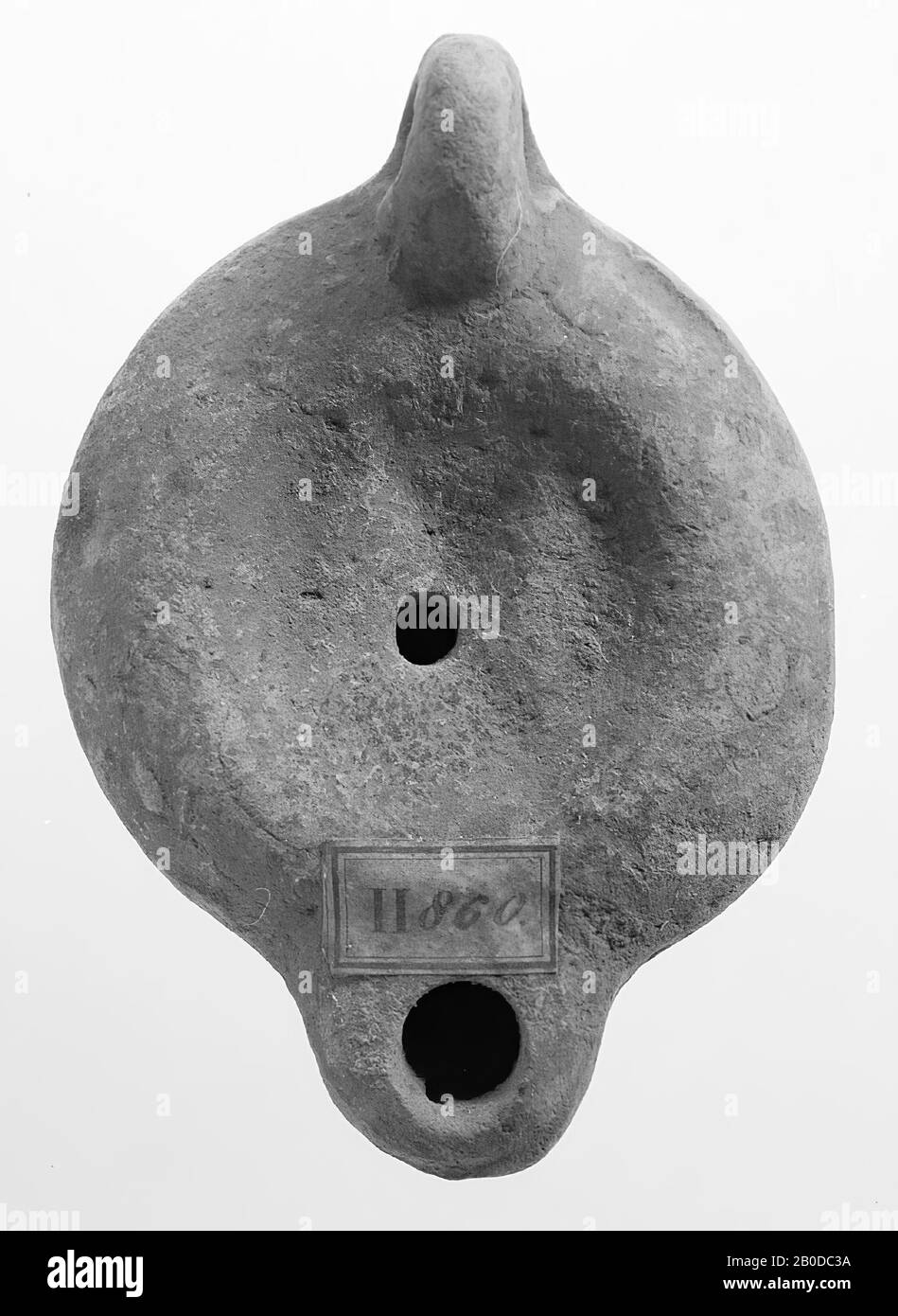 Eine Lampe aus rotem Steingut mit runder Karosserie auf runder Basis. Der runde, konkave Spiegel ist von einem eingelassenen Kreis umgeben und mit einem undeutlichen Reliefbild verziert. Das kleine Füllloch befindet sich in der Mitte. Der kurze, stumpfe Ausguss ist flach und rund geschlossen und hat ein kleines Feuerloch. Das senkrecht angebrachte Ohr war mit Kerben, Öllampe, Steingut, Terrakotta, 4,2 x 9,6 x 6,7 cm, 2. Hälfte 1. Jahrhundert bis 1. Hälfte 3. Chr. dekoriert. 50-250 n. Chr., Tunesien Stockfoto