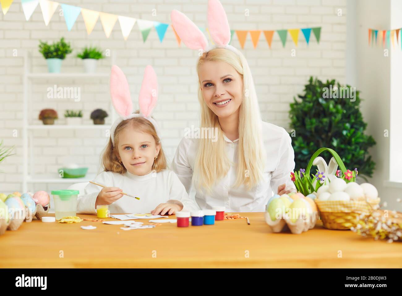 Frohe ostern. Tochter und Mutter mit Kaninchenohren schmücken an einem Tisch sitzende Ostereier Stockfoto