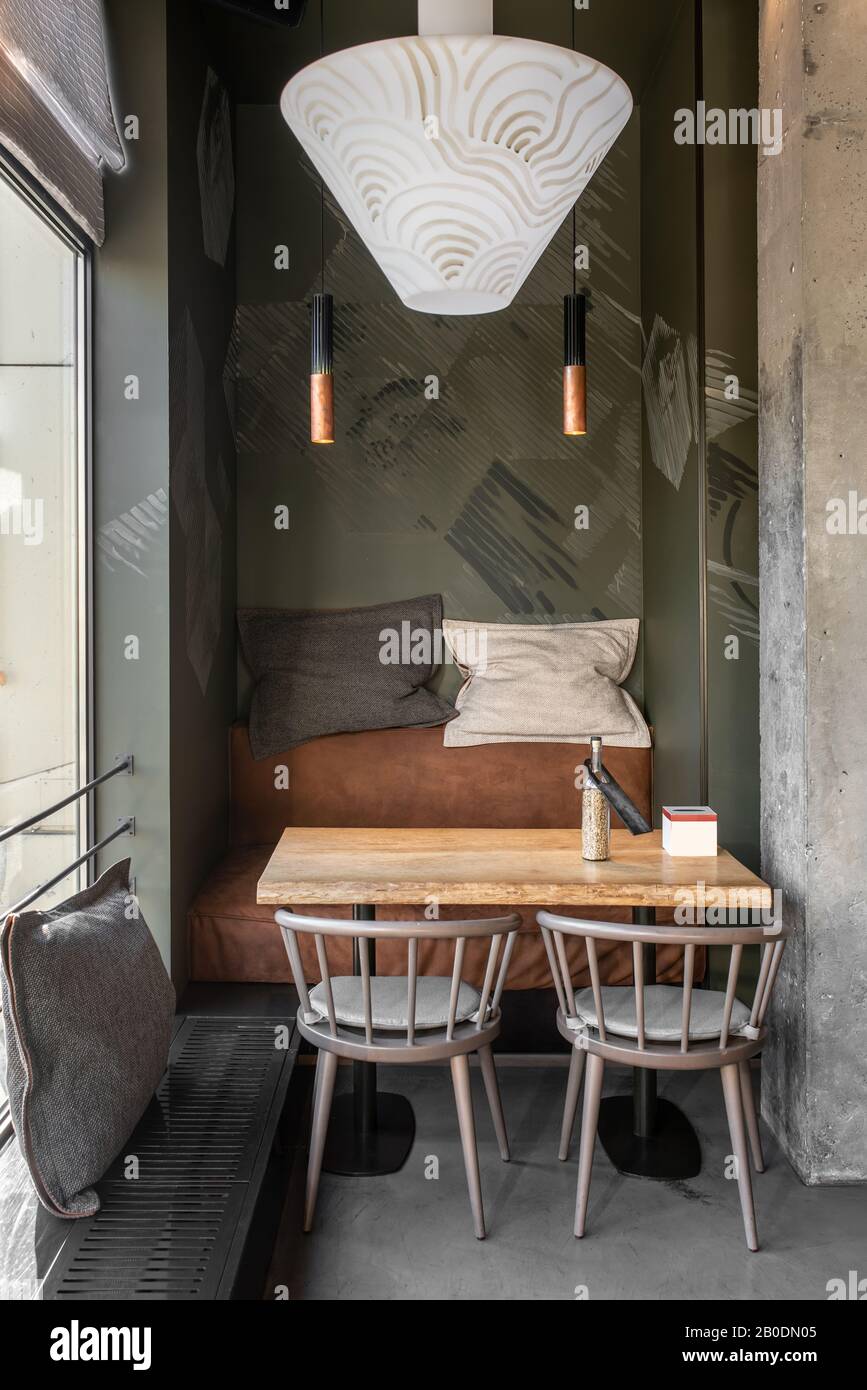 Café im Loft-Stil mit Strukturwänden und Betonsäule. Es gibt einen Holztisch mit Sofa und Stühlen, Kissen, Fenster mit einem Vorhang, hängend Stockfoto