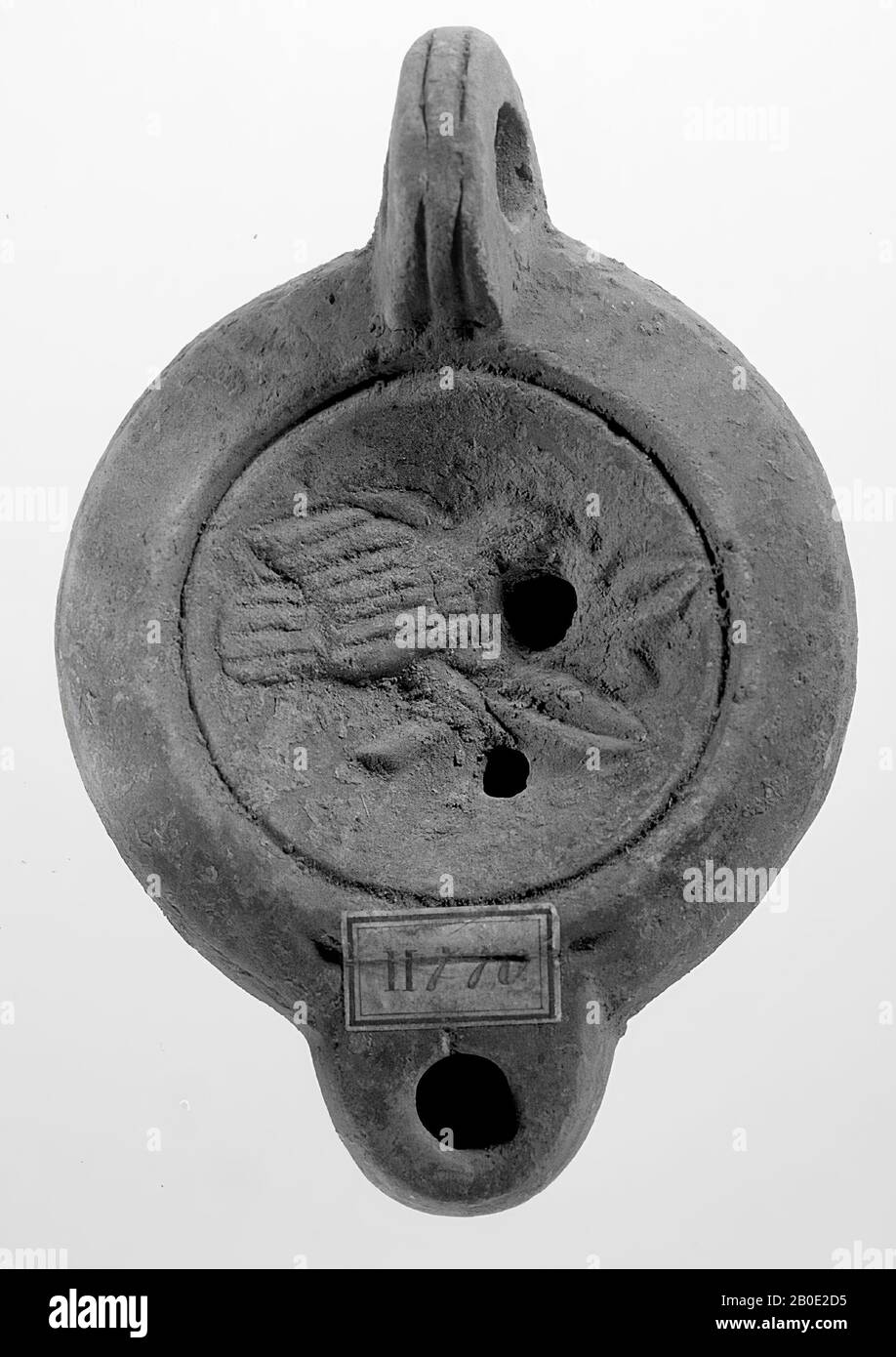 Eine braun lackierte Lampe mit rundem Körper auf runder Basis. Der runde, konkave Spiegel ist von konzentrischen Kreisen umgeben und mit einem Reliefbild eines Vogels verziert, der auf einem Ast sitzt. Unter dem Vogelkopf befindet sich ein kleines Füllloch. Unter dem Ast befindet sich ein zweites Füllloch. Der kurze, stumpfe Ausguss ist rund und hat ein kleines Feuerloch. Das senkrecht angebrachte Ohr ist mit Kerben verziert. Am Anfang des Auswurfkrümmers befinden sich auf beiden Seiten zwei eingezogene Punkte: Öllampe, Steingut, Terrakotta, 4,5 x 10,7 x 7,4 cm, 2. Hälfte 1. Jahrhundert bis 2. Hälfte 3. Chr. 50-250 n. Chr., Tunesien Stockfoto