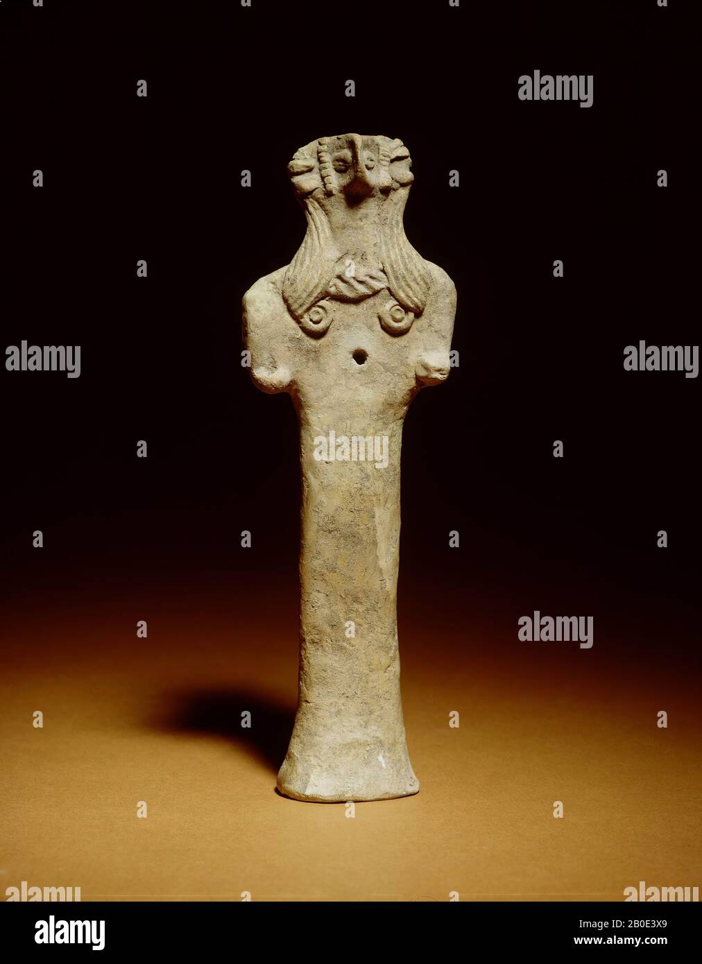 Kühle Terrakotta-Figur auf einem konkaven Boden mit einem - Querschnitt - ovalen, säulenförmigen Körper (mit einem jüngeren Loch vorne). Der Kopf hat eine rechteckige, beakige Nase und kaffebohnenförmige Augen und ist auf beiden Seiten weiter mit zwei senkrechten Bändern und drei aufgesetzten Ohrdekorationen verziert. Zwei breite Haarbänder fallen über die Schultern und enden in kreisförmigen Locken. Zwischen den Haarbändern ein Ausschnitt mit doppeltem Fischgrätmuster. Die Arme sind als Knötchen dargestellt, die rechte ist durchbohrt. Auf der Rückseite des Kopfes eine breite, dreieckige Projektion. Auf der Rückseite eine geometrische Dekoration aus inkisierten Linien. Die Stockfoto