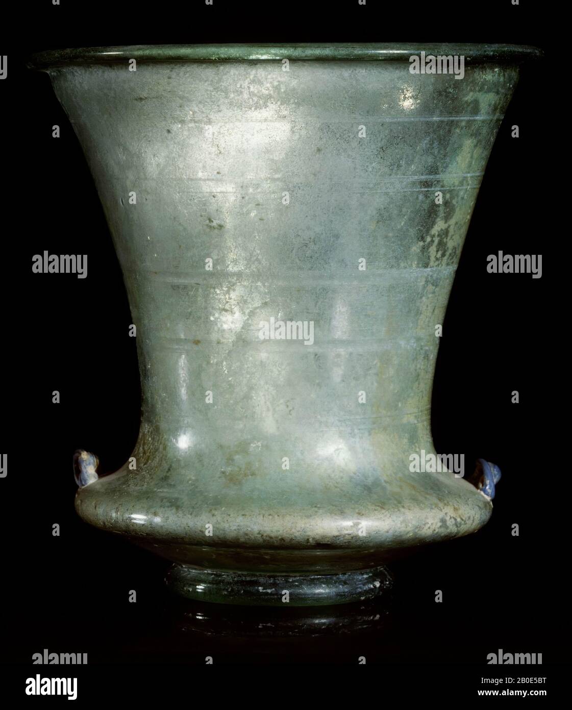 Dieser perfekt geformte Kelch steht in der Tradition des Schaukeles, den die Römer Karchesium nannten. Das hellgrüne Glas besteht aus extrem dünnwandigen. Die Dekoration besteht aus Mini-Ohren aus Ultramarin Glas auf der Schulter und einigen geschliffenen horizontalen Bändern auf dem oberen Teil des Carchesiums. Der eigentliche Vasenkörper besteht aus einer Schicht und stark konvexem Teil, der sich in einen elegant geformten, ausgestellten Kelch verwandelt. Die Form steht am Übergangspunkt zweier Welten: Zum einen steht das Stück in der Tradition des römischen Showcups, zum anderen weist es auf den Glanz islamischen Glases hin Stockfoto