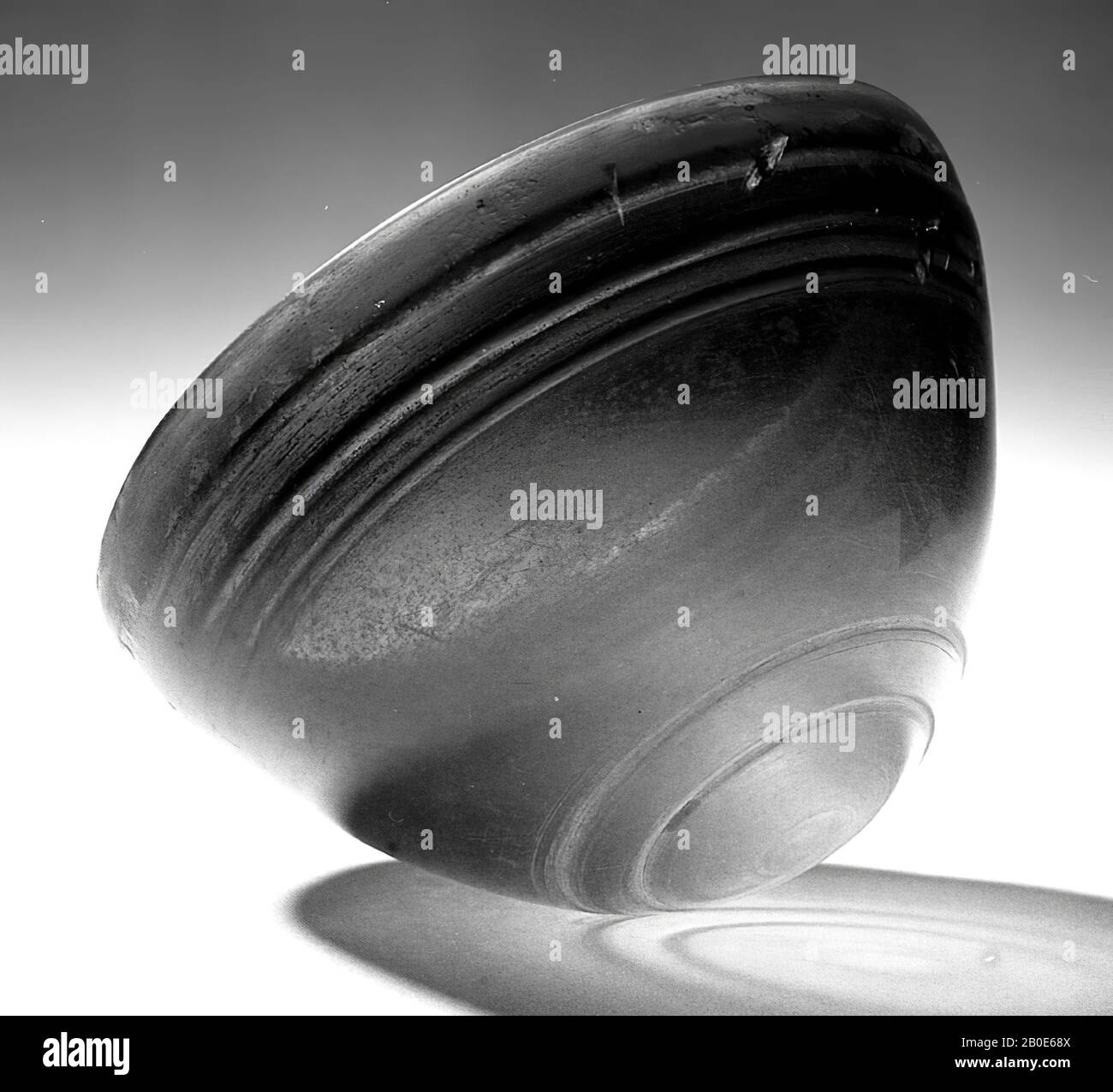 Die Technik des Glaspressens ermöglichte es erstmals, Trinkgeschirr in diesem Material zu tragen. Diese hellenistische Trinkschale stammt aus Syrien, einem Gebiet mit einer langen Glastradition. Die Schüssel besteht aus Bernsteinglas. Nach dem Einpressen einer Form wird die Schüssel poliert und mit Rillen entlang der Unterseite und Kante eingraviert. Der ursprüngliche Glanz der Oberfläche ist erstaunlich gut erhalten. Die Form ähnelt stark den hellenistischen Schalen aus Steingut, die als "megarische Becher" bezeichnet werden. Diese Art von Steingut wird auch in Formen gebildet. Das Stück kann nicht allein stehen: Auf dem Tisch Stockfoto