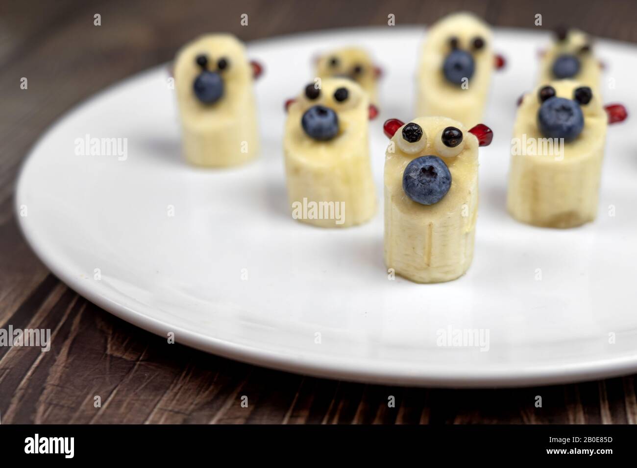 Lustige kleine Bananen tragen Figuren auf weißem Teller gesundes Dessert für Kinder. Stockfoto