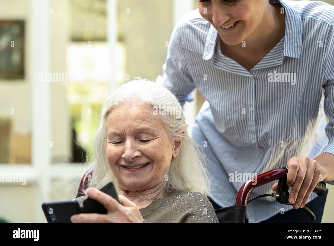 Ältere Patientin, die dem jungen Hausärmer ein Mobiltelefon vorführt Stockfoto