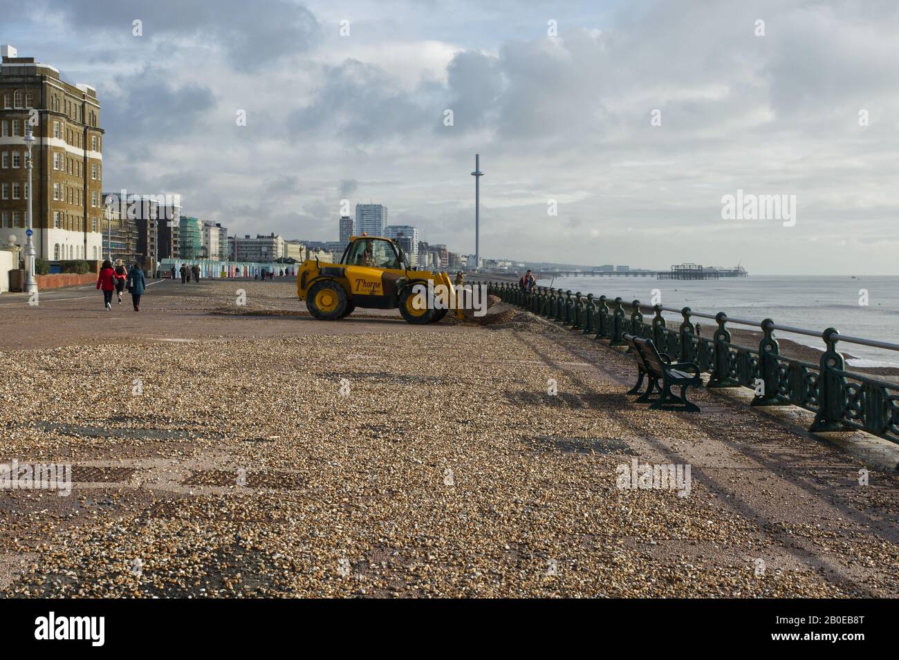 Sturmschäden an der Küste mit Schindeln über Promenade und Straße in Brighton und Hove in East Sussex, England. Mit einem Ausgräber, der Steine zurückbewegt. Stockfoto