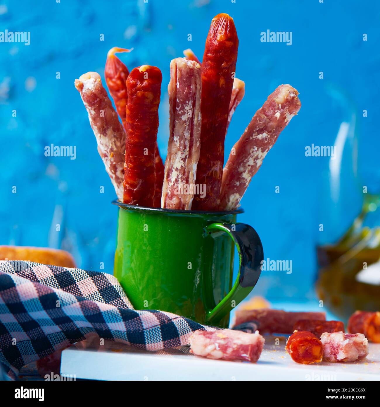 Einige Fuet- und Chorizo-Stücke, zwei verschiedene spanische Wurstwaren in einem grünen Becher auf einem Tisch, neben einigen Brotscheiben und einem Grausamkeiten mit Oliven Stockfoto