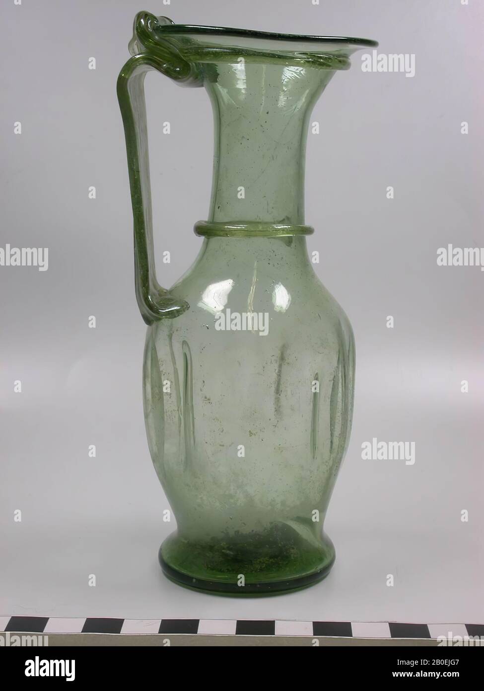 Glas olivgrünes Glas mit gefaltetem Bauch. Hübscher langer Hals mit trompetenförmigem Mund, bandförmigem Ohr und Ringen um Hals und Mund, Kanne, Glas, 15,8 cm, IV Stockfoto