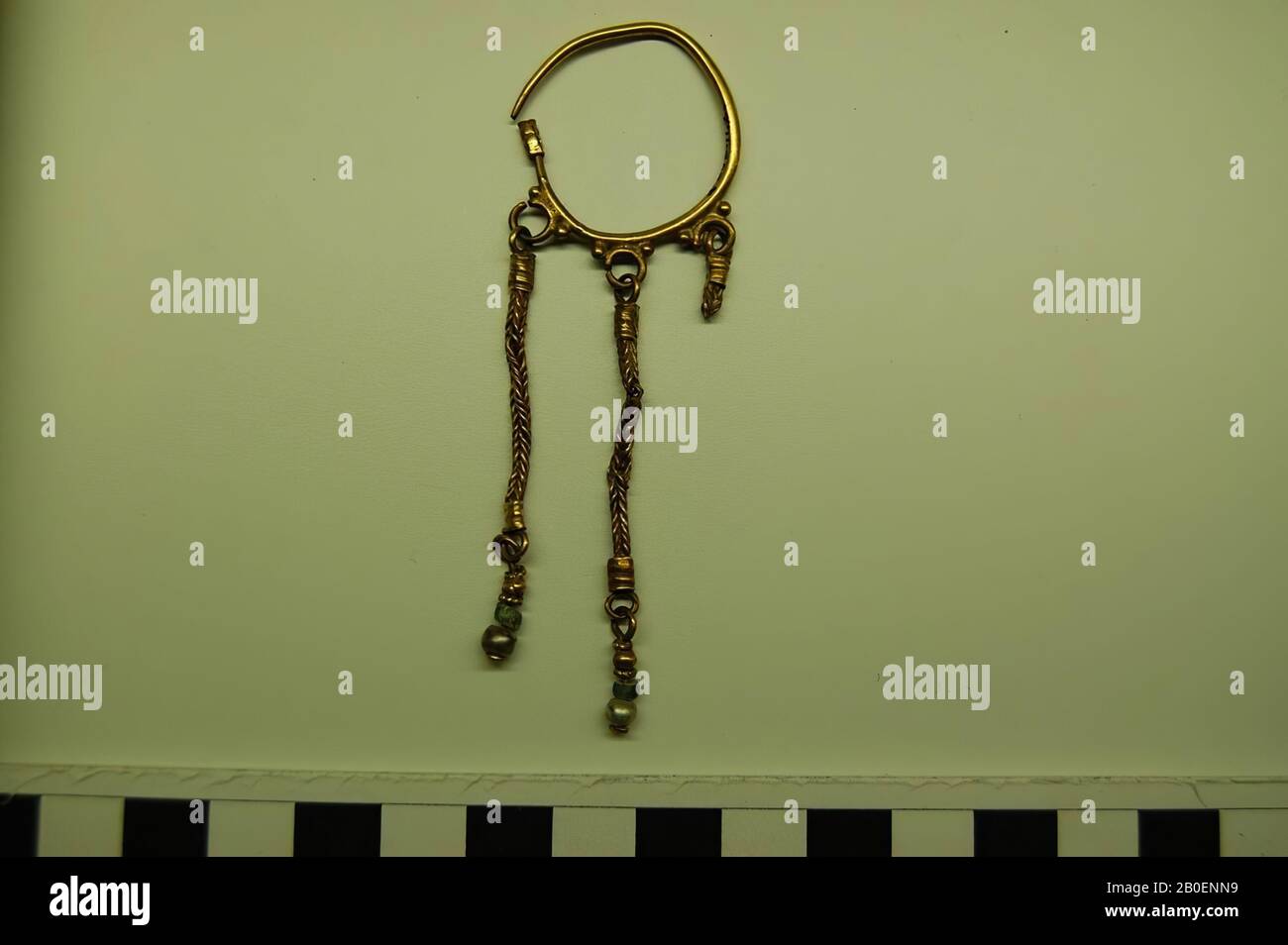 Ein großer goldener Ohrring mit drei Ringen, die an geflochtenen Goldketten mit goldenem Perlen, einem Perlen aus grünem Glas und einer Perle hängen., Ohrring, Gold, Perle, Glas, 2,9 x 9 cm, 100 Stockfoto