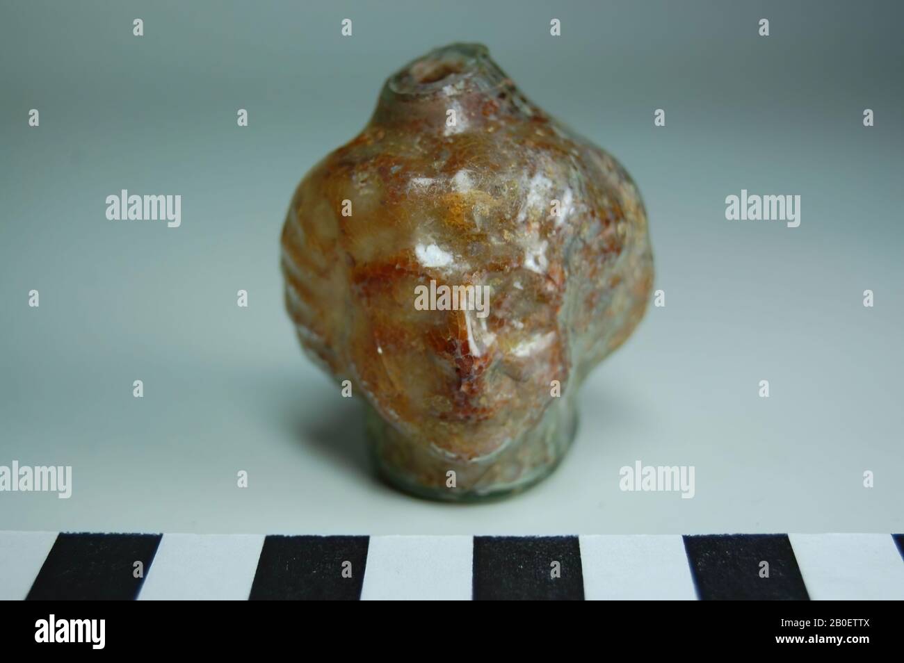 Figurenvase, Kopf, Weibchen, Bilden Geblasene Parfümflasche aus transparentem grün-braunem Glas. Die Flasche hat einen Körper in Form von zwei Gesichtern von hinten nach hinten, solche Flaschen werden auch "Janus"-Kopfflaschen genannt. Das Stück wird in eine Doppelform geblasen, die Malnaad ist auf Basis und Boden gut sichtbar. Die Gesichter sind nicht ganz gleich, eine ist in schärferer Erleichterung geblasen als die andere. Das Haar ist in einem einheitlichen Muster von Graten stilisiert, die in Reihen um das Gesicht angeordnet sind. Der Fuß ist mit senkrecht ausladenden Graten verziert, die geprägt sind, der Flaschenhals ist gebrochen., Vase, Figurenvase, Glas Stockfoto