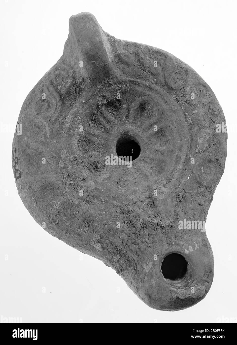 Eine Lampe aus rotem Steingut mit einem ovalen Körper auf einem runden Sockel. Der runde, konkave Spiegel ist von konzentrischen Kreisen mit dem kleinen Loch in der Mitte umgeben und mit einer kleinen achtblättrigen Rosette verziert. Die Schulter ist mit einem Flechtband verziert. Der kurze, abgerundete Ausguss hat ein kleines Feuerloch und ist mit Palmetten verziert. Der senkrechte Griff ist am unteren Ende sowie der Ausguss verziert. Marke: Sehr schöne Fußsohle, Öllampe, Keramik, Terrakotta, 2,7 x 6,7 x 4,7 cm, 3. Und 4. Jahrhundert n. Chr. 200-400, Asien Stockfoto