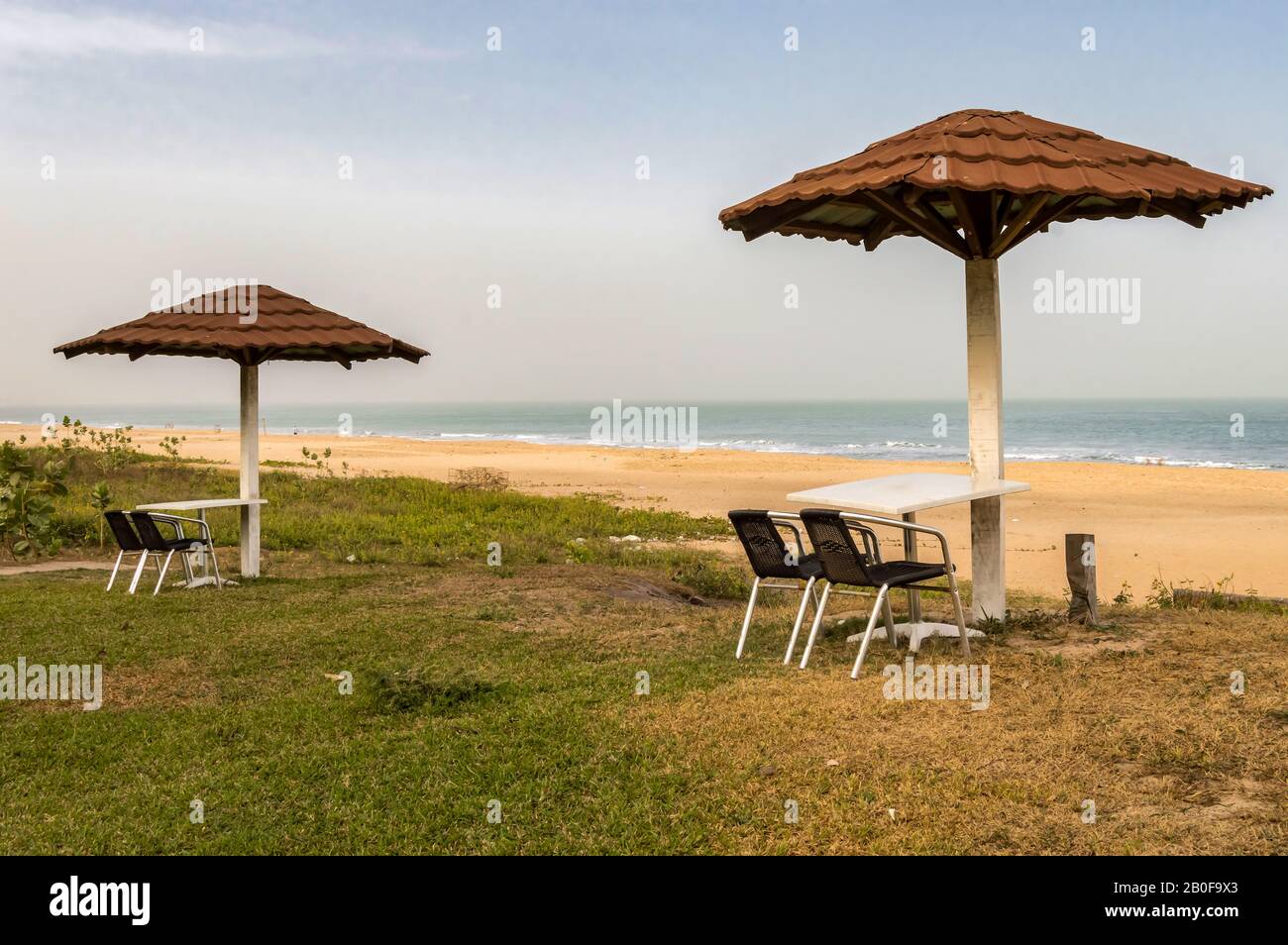 Zwei Stühle und ein Tisch liegen zum Meer, knapp unter einem roten Fliesenschirm an einem Strand in Gambia Stockfoto