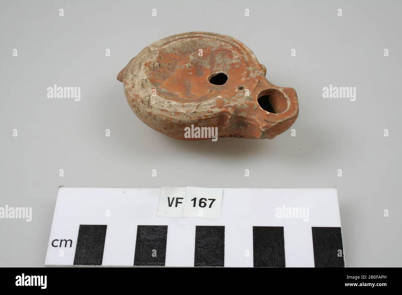 Ohrenleuchte mit verziertem Spiegel. Loeschcke Typ I B, Schulterform I (2 Rillen). Weiße Erde mit orangefarbenem Anstrich. Ohr abgebrochen. Schulter links beschädigt. Füllen Sie das Loch direkt unter der Mitte. Feuerloch. Standfläche. Runder Luftspalt. Präsentation auf dem Spiegel: Bulle von einem Bären, Öllampe, Steingut, 8 x 5,3 x 2,5 cm, roman 15-50, Niederlande, Utrechter, Bunnik, Vechten, Houtense Vlakte angegriffen Stockfoto