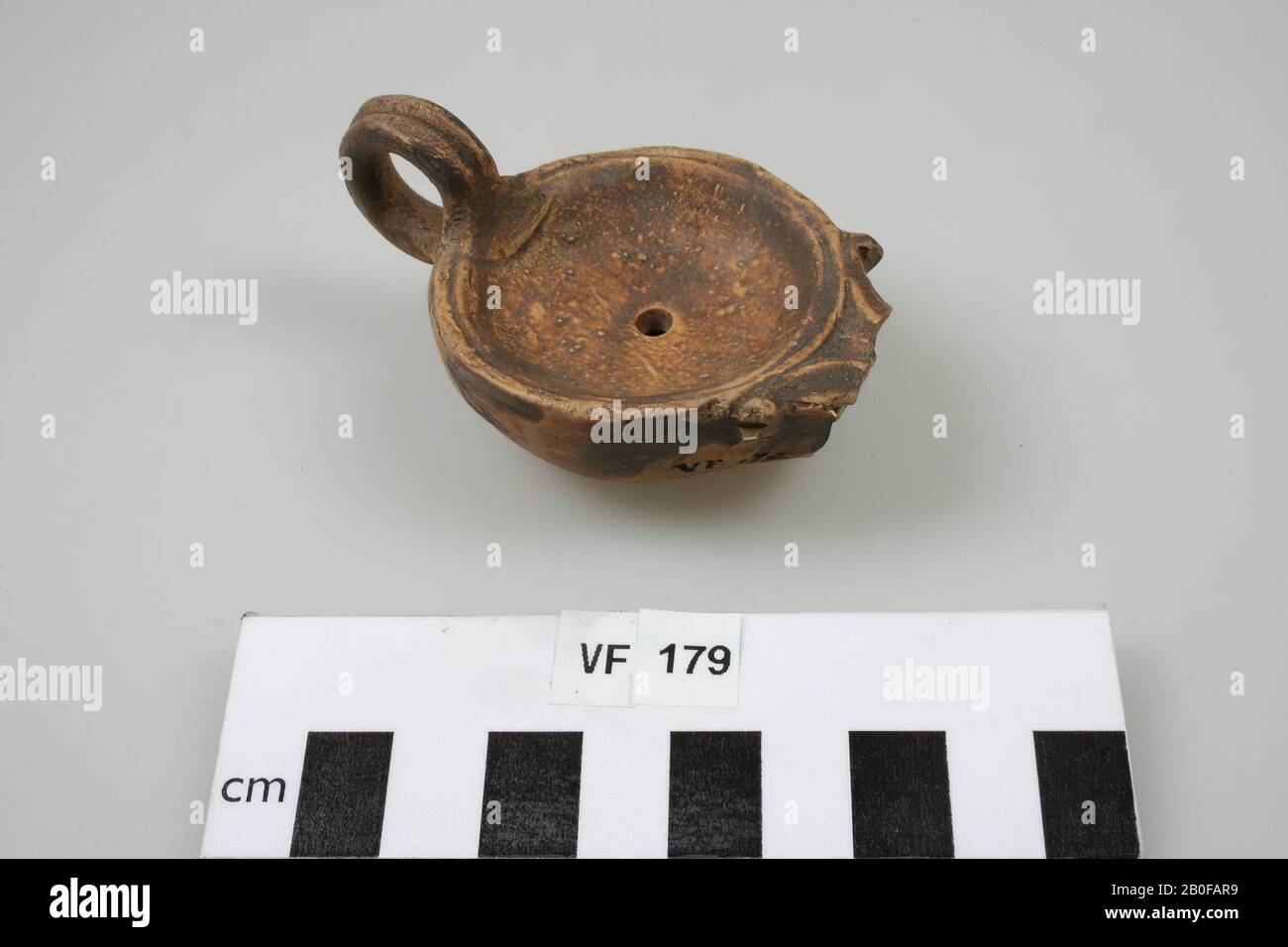 Ohrenleuchte mit schmucklosem Spiegel. Loeschcke Typ I oder IV oder Leibundgut III, Schulterform mit einer Nut. Cremefarbene Erde mit hellbrauner bis dunkelbrauner Farbe. Ausguss abgebrochen, zweiteiliges Ohr, Füllloch im mittleren, stehenden Bereich. Keine Darstellung auf dem Spiegel., Öllampe, Keramik, 8 x 5,1 x 3,5 cm, roman 15-50, Niederlande, Utrechter, Bunnik, Vechten, Houtense Vlakte Stockfoto