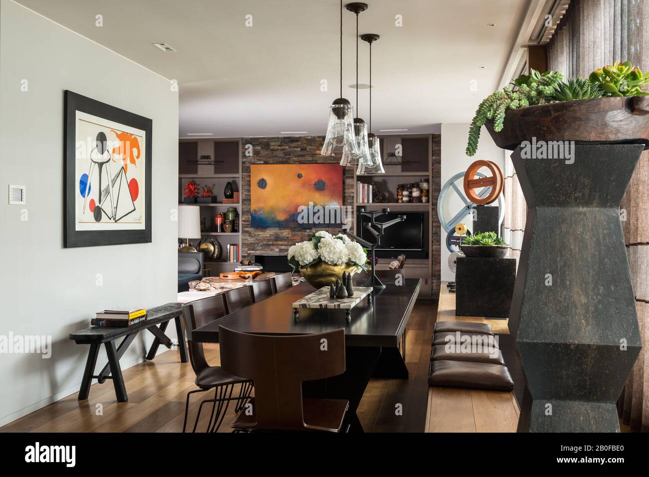 Pendelleuchten aus Glas über dem Tisch mit modernen Kunstwerken und Schieferwänden in einem offenen WestLondoner Apartment. Stockfoto