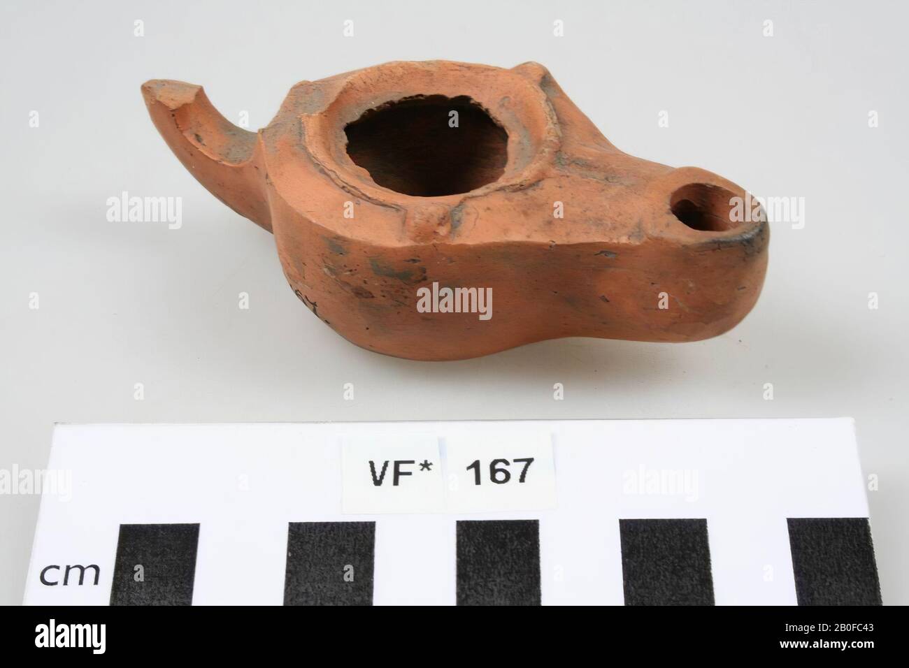 Ohrenleuchte mit verziertem Spiegel. Loeschcke Typ I B, Schulterform I (2 Rillen). Weiße Erde mit orangefarbenem Anstrich. Ohr abgebrochen. Schulter links beschädigt. Füllen Sie das Loch direkt unter der Mitte. Feuerloch. Standfläche. Runder Luftspalt. Präsentation auf dem Spiegel: Bulle von einem Bären, Öllampe, Steingut, 8 x 5,3 x 2,5 cm, roman 15-50, Niederlande, Utrechter, Bunnik, Vechten, Houtense Vlakte angegriffen Stockfoto