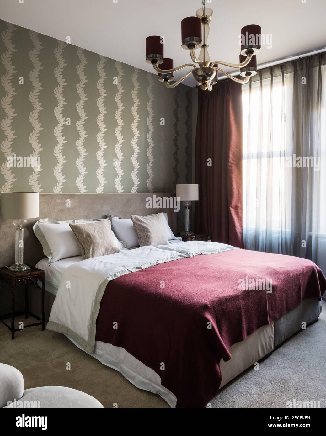 Burgunderdecke auf Doppelbett mit Vintage-Beleuchtung und geschlossenen Vorhängen Stockfoto