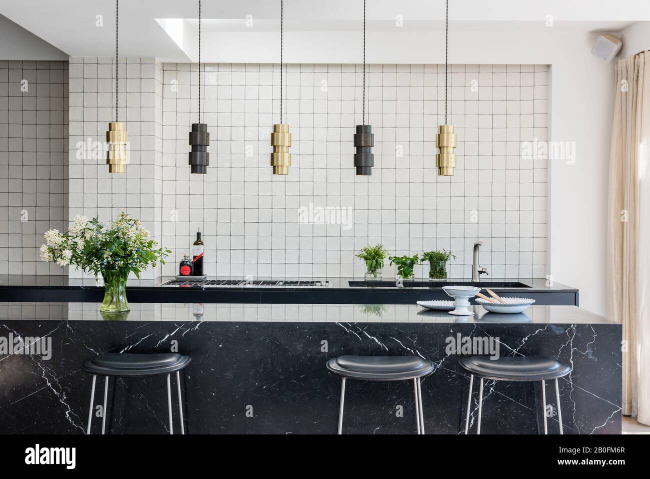 Nero Marquina Granit Arbeitsplatte mit Bronze- und Messingring Hängeleuchten von CTO und Gitter aus weißen Fliesen Stockfoto