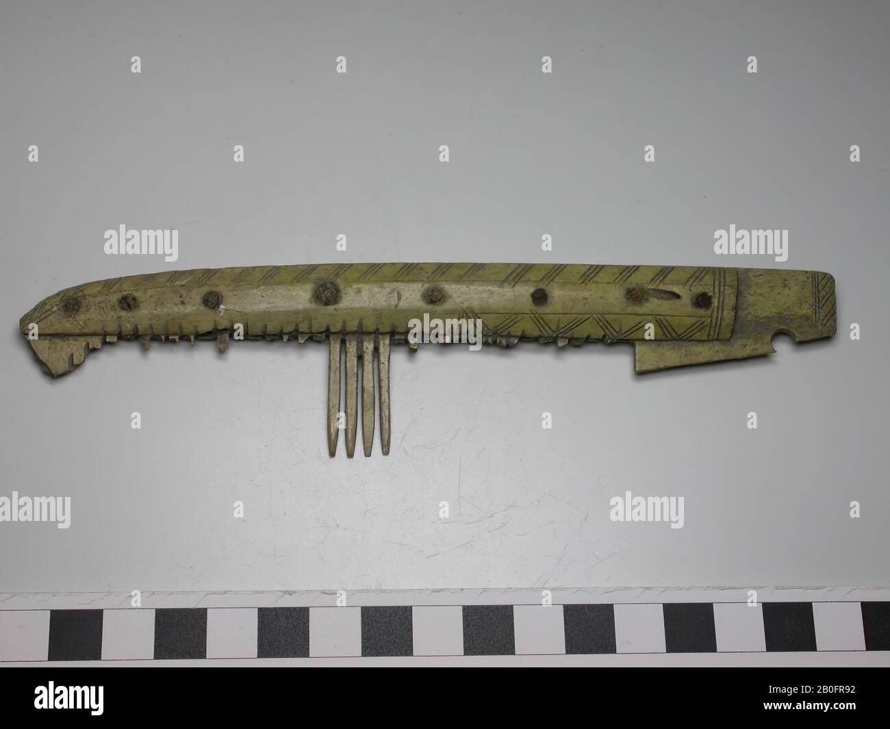 Einseitiger dreilagiges Kammaufsatz. Typ: Asymmetrischer Kamm mit einer rechteckigen Platte am Ende Dekoration: Griffblatt: Horizontale Linien, schräge, kurze vertikale Linien und Sägezahnschmuck (die aus Doppellinien besteht). Ein Griffblatt ist undekoriert. Rechteckige Platte: Vertikale Linien und karierte Motive. Form: Gerade Basis. Die Oberseite ist gerade, aber das Ende hat eine gebogene Form. Die Platte, die als Griff dient, ist rechteckig. Zahnplatten: 5. Endplatten: 1 (auf der anderen Seite befindet sich der Griff). Ursprüngliche Anzahl der Zahnplatten: 7. Zähne: 4 ganze Zähne (leicht abgenutzt). Degradierte Zähne: 31 Stockfoto