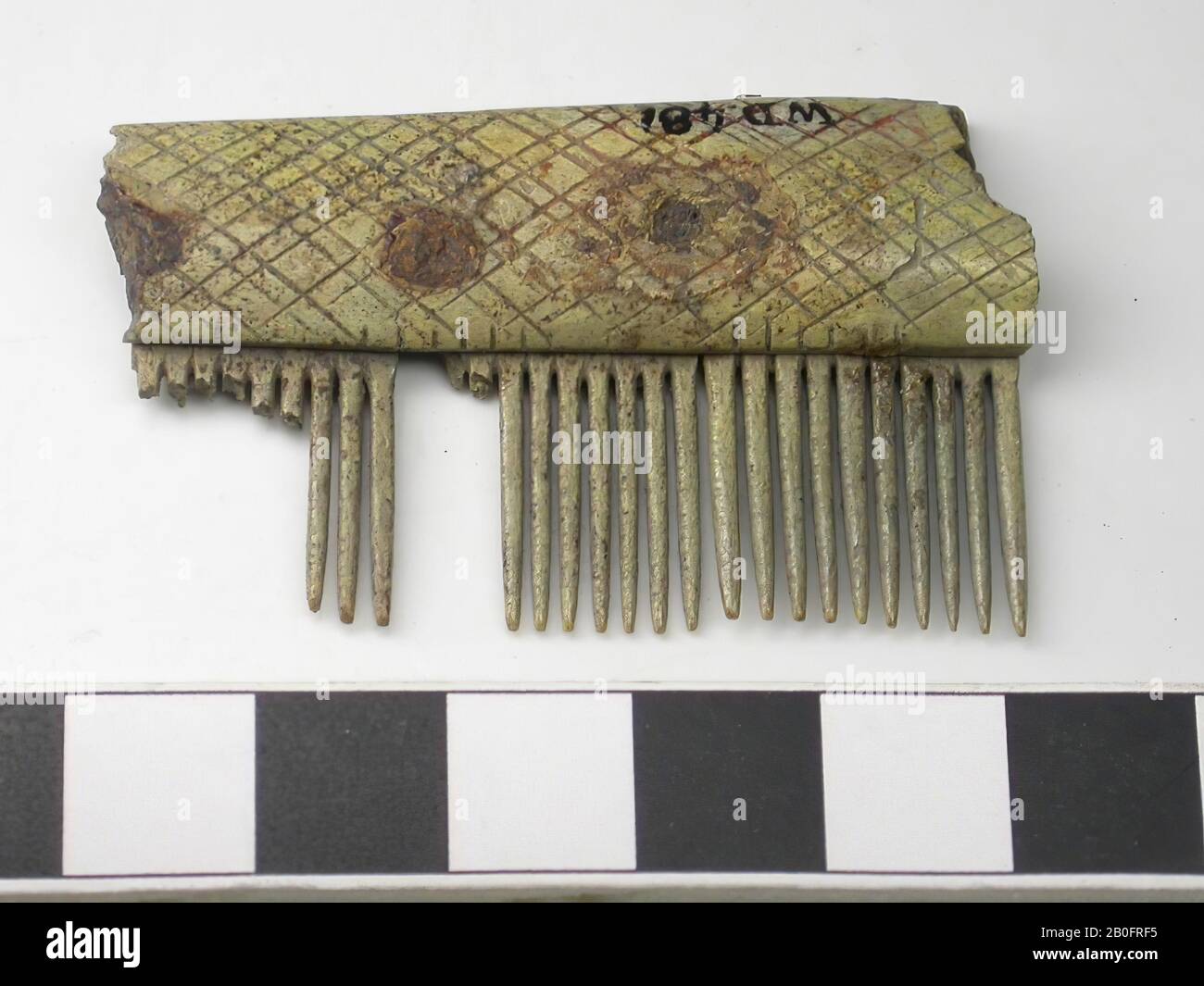 Bruchstück einer Griffklinge mit einer Reihe von Zahnplatten eines einseitigen dreilagigen Kamms. Typ: Mehrere Möglichkeiten: Langer Kammaufsatz, Flügelkamm, Kammaufsatz? Dekoration: Rautenmuster. Form: Gerade Basis, leicht gebogenes Oberteil. Dünne Griffklinge. Zahnplatten: 3. Endplatten: 0. Zähne: 20 ganze Zähne (leicht verschlissen). Gebrochene Zähne: 8. Ursprüngliche Anzahl der Zähne: Unbekannt. Ein Teil einer Griffklinge und 3 Zahnplatten sind erhalten geblieben. Sägemarke: So wurden zuerst die Zahnplatten und die Griffblätter aneinander befestigt und dann die Zähne eingesägt., Kammfragment, organisch, antler, l = 5,1 cm und b Stockfoto