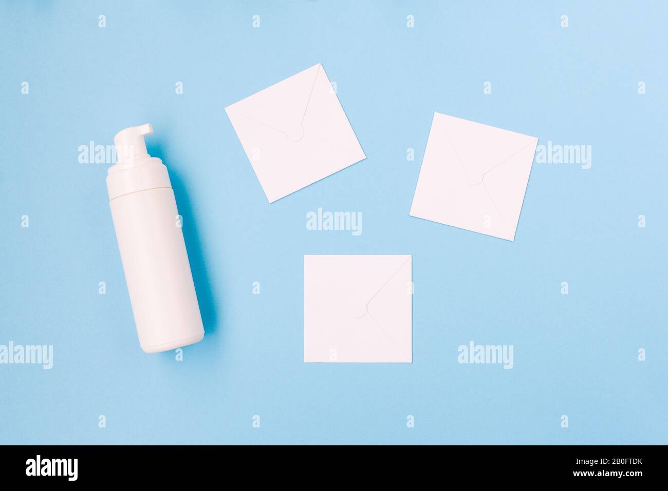 Schaum zum Waschen und weiße Papierblätter auf blauem Hintergrund. Weiße Kunststoffflasche. Kosmetische Produkte für Körper- und Gesichtspflege mit Kopierraum Stockfoto