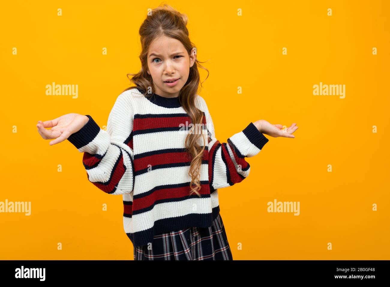 Niedliches Mädchen im legeren gestreiften Pullover, das Arme auf orangefarbenem Hintergrund winkt Stockfoto