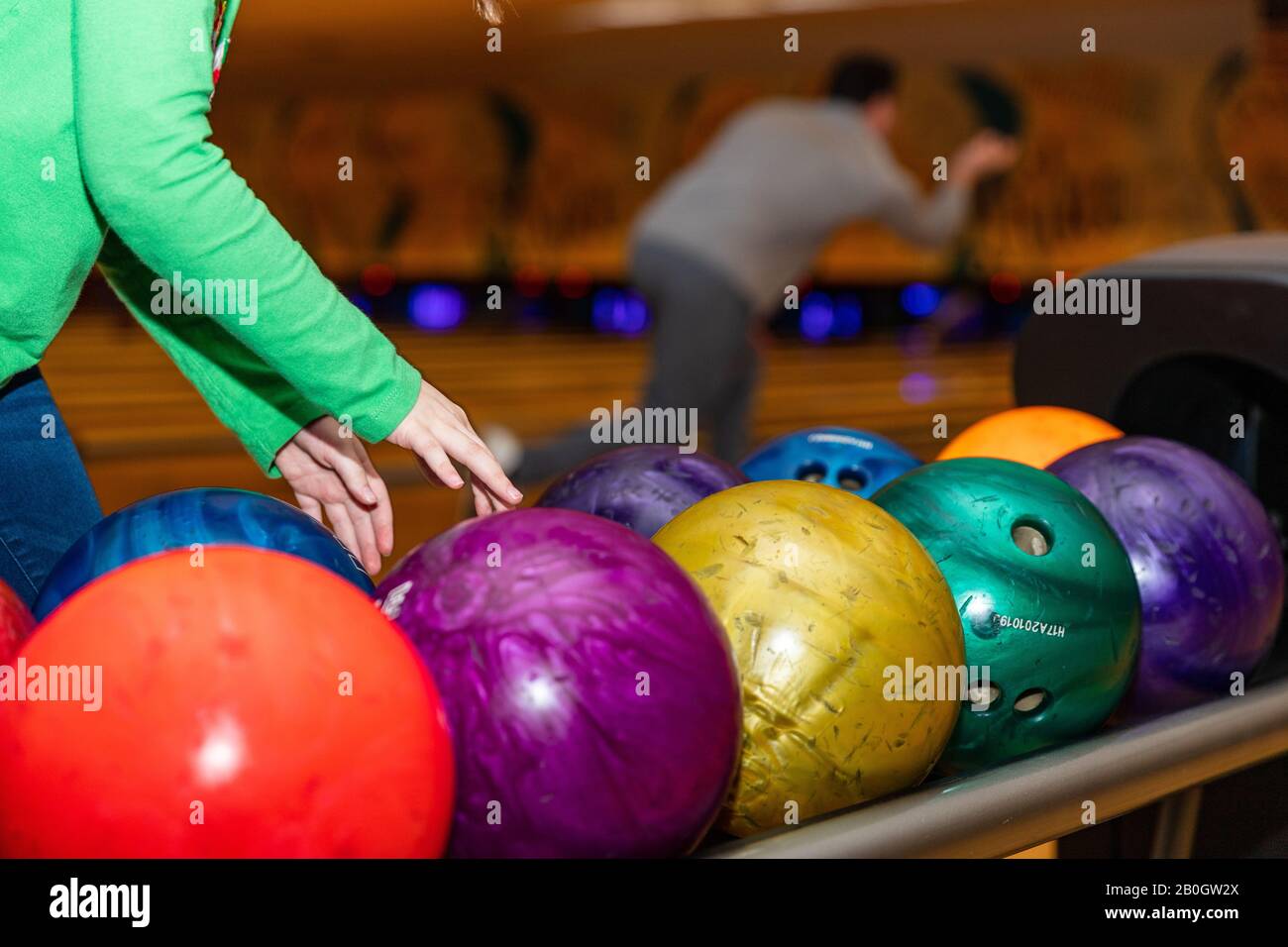 Die Hände des Kindes reichen, um den Bowlingball in der Bowlingbahn aufzunehmen Stockfoto