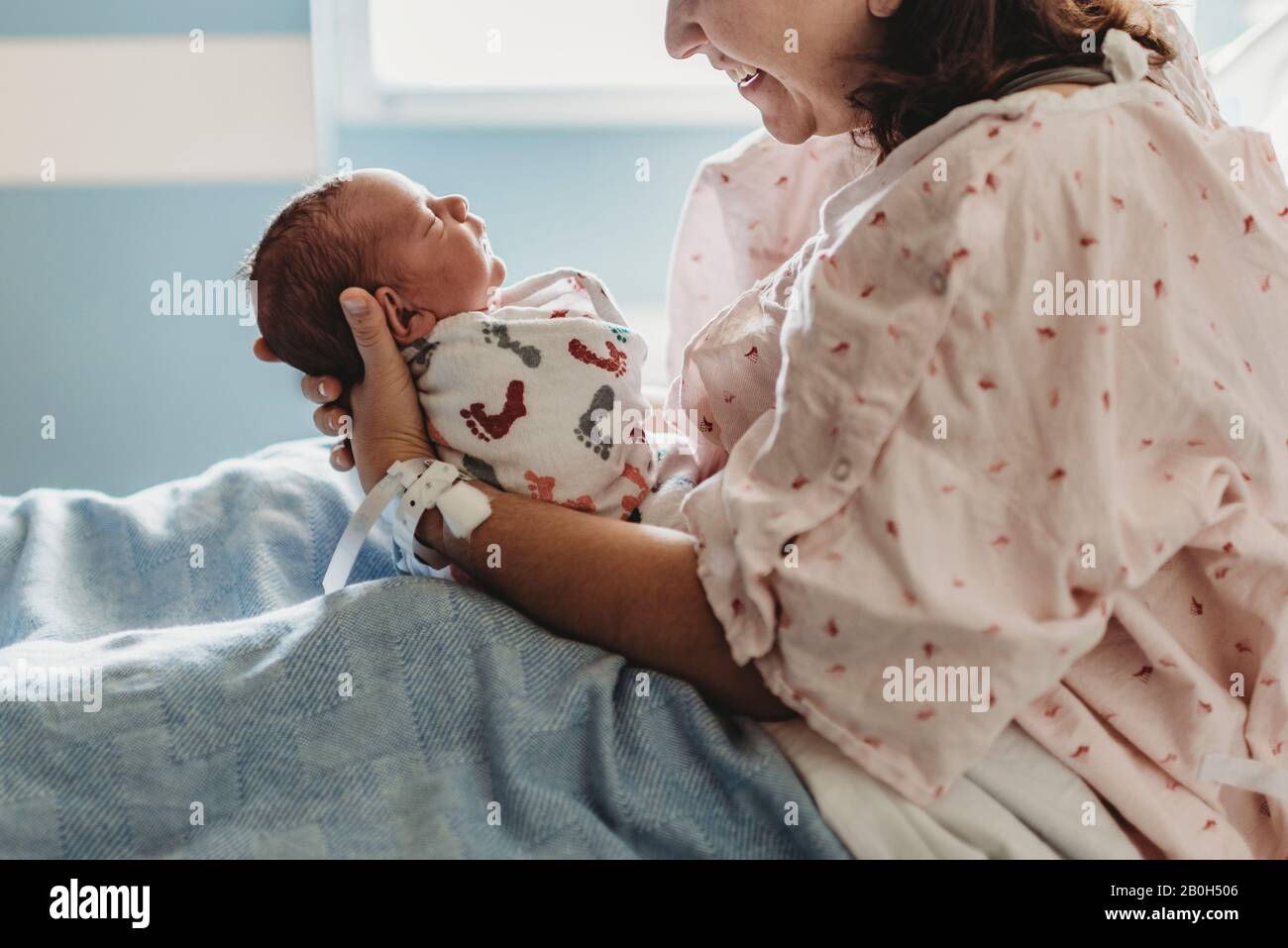 Seitenansicht der Mutter, die im Krankenhaus den neugeborenen Sohn anlächelt und anschaut Stockfoto