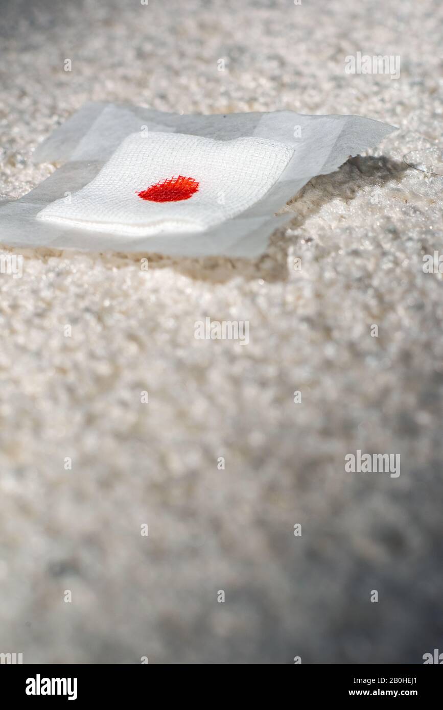Gestürzter Verband mit Blutfleck auf weißem Teppich. Stockfoto