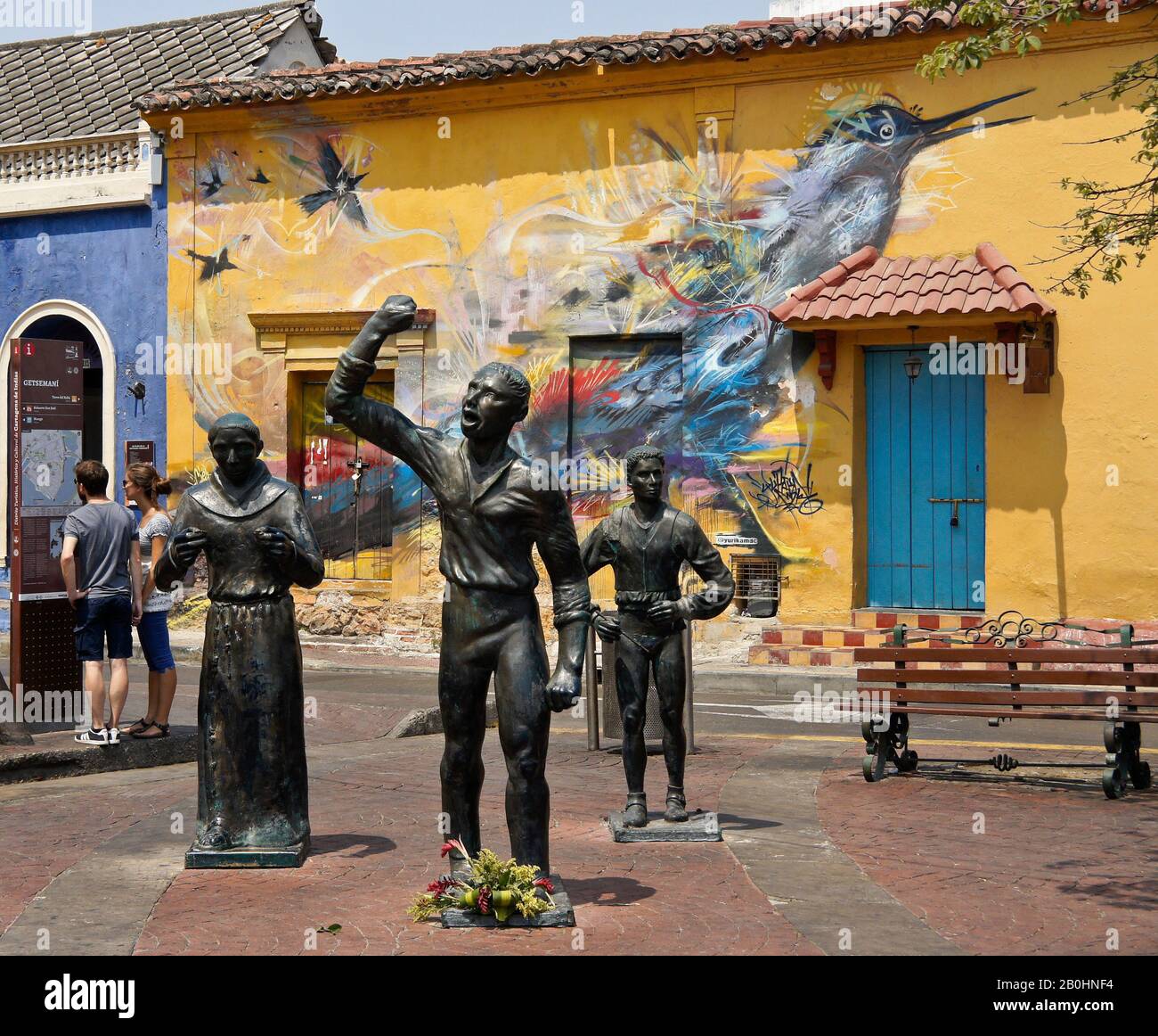 Skulpturen von Unabhängigkeitshelden auf der Plaza Trinidad gegenüber der Straßenkunst, die ein Kolonialgebäude in Getsemani, Cartagena, Kolumbien schmückt Stockfoto