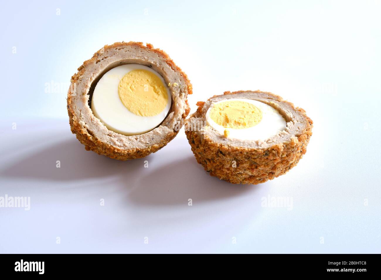 Scotch Egg in einem halben traditionellen herzhaften Imbiss, bestehend aus einem hart gekochten Ei, umgeben von Wurstfleisch und Brot-Krümel-weißem Hintergrund Stockfoto