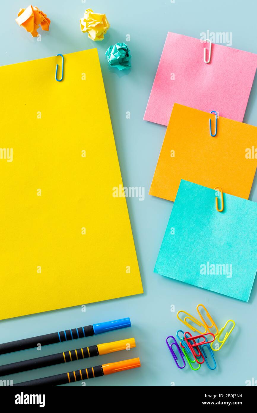 Gelber Wecker auf einer violetten Karte mit der Aufschrift "geschäftig Tag" farbige Büroklammern, Karten, Stifte, zerknitterte Papierkugeln. Platz für Text Stockfoto
