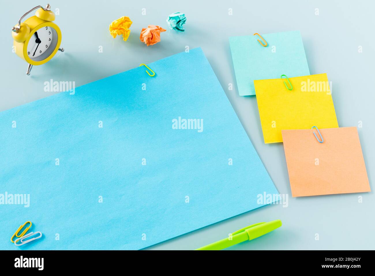 Gelber Wecker auf einer violetten Karte mit der Aufschrift "geschäftig Tag" farbige Büroklammern, Karten, Stifte, zerknitterte Papierkugeln. Platz für Text Stockfoto