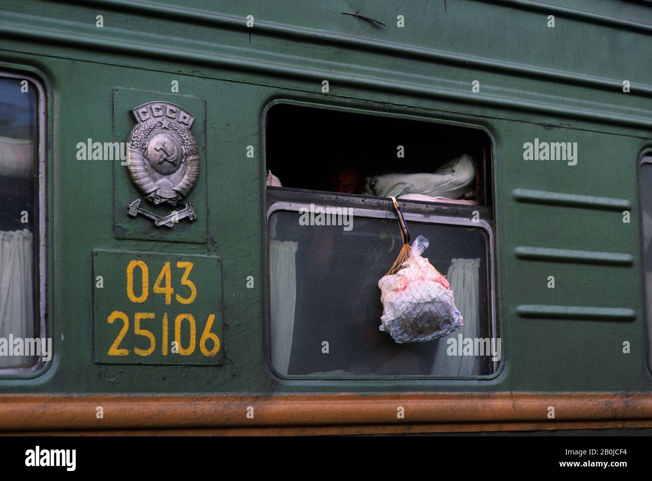 RUSSLAND, SIBIRIEN MOGOCHA, TRANSIBIRISCHE ZUGSZENE MIT MENSCHEN, DIE LEBENSMITTEL AUS DEM ZUGFENSTER HÄNGEN, UM KÜHL ZU BLEIBEN Stockfoto