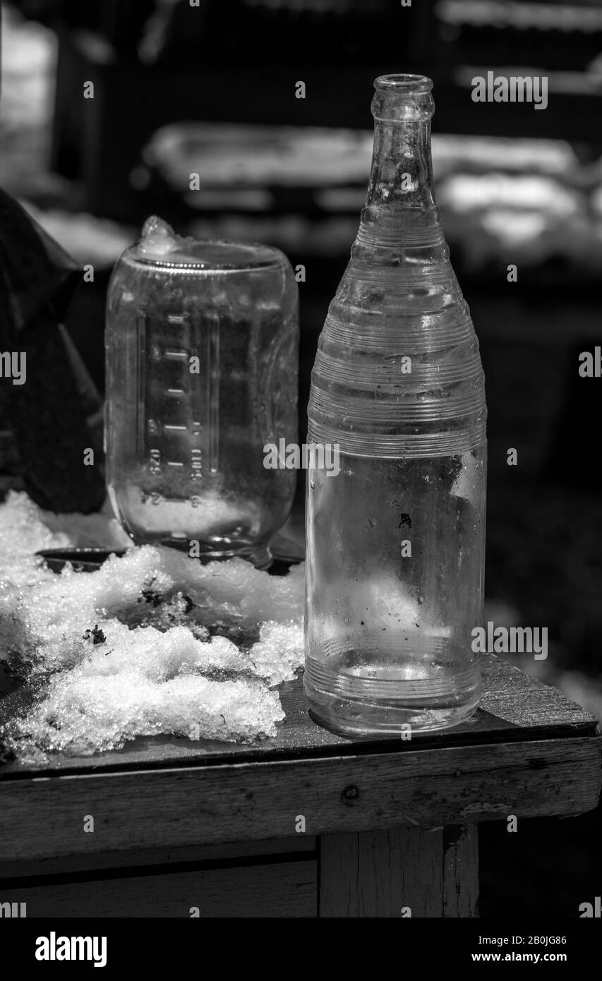 Antike Flasche und Krug ruhen im Schnee auf einem alten Holztisch im Freien Stockfoto