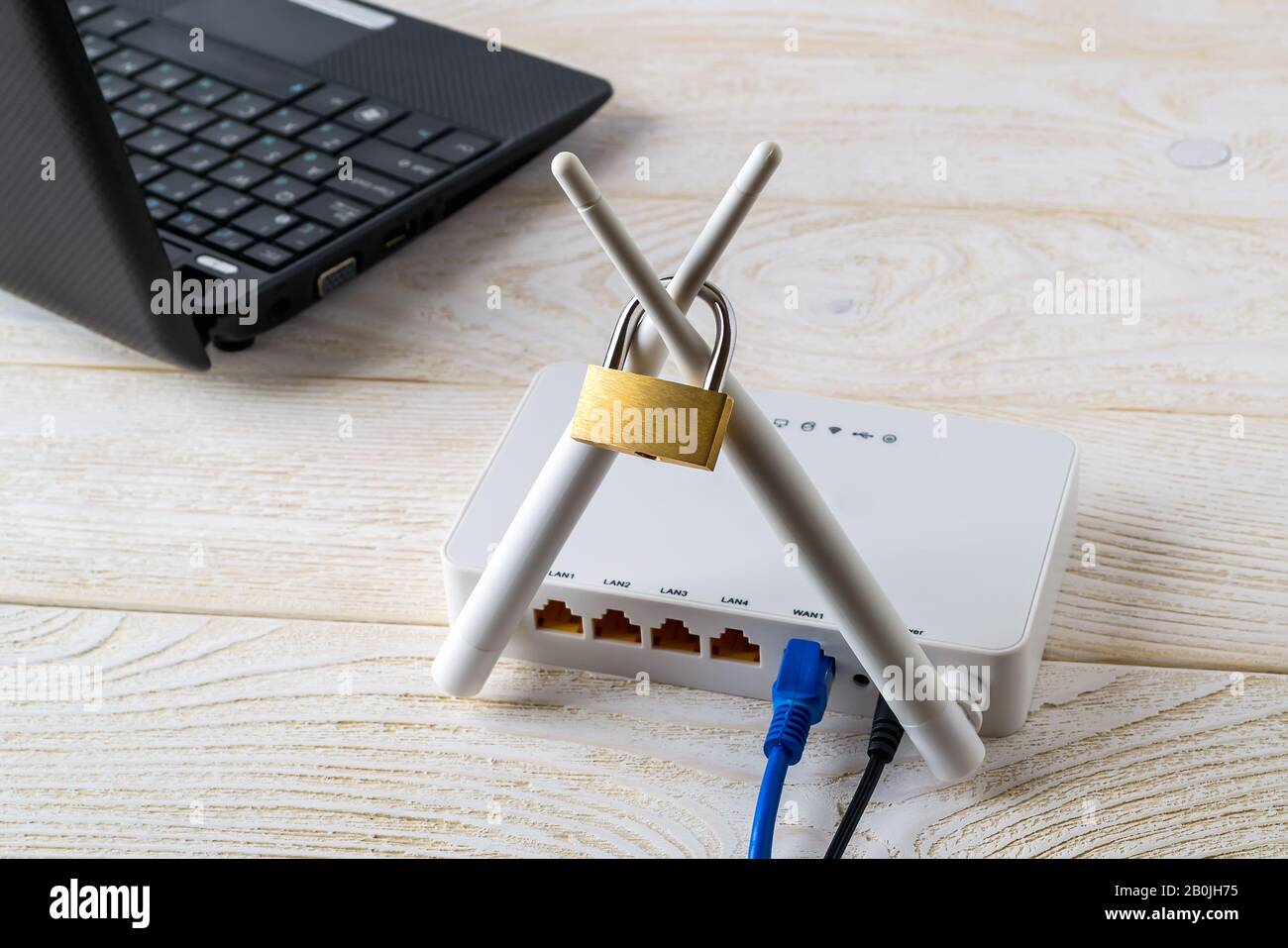 Weißer WLAN-Router mit Vorhängeschloss auf Antennen in der Nähe des Laptops über Holztisch. Verbotene oder eingeschränkte Konzepte der Internet- und Internetzensur. Stockfoto