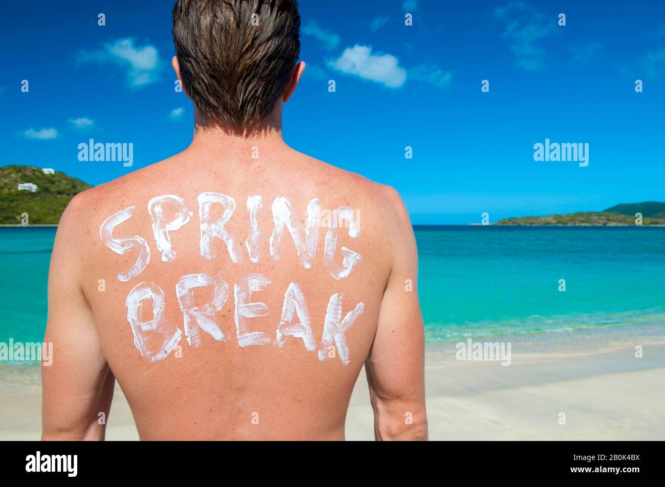 Junger Mann mit der Nachricht "Spring Break", die auf dem Rücken in Sonnenschutzmaske geschrieben wurde und über den Horizont der tropischen Insel blickt Stockfoto