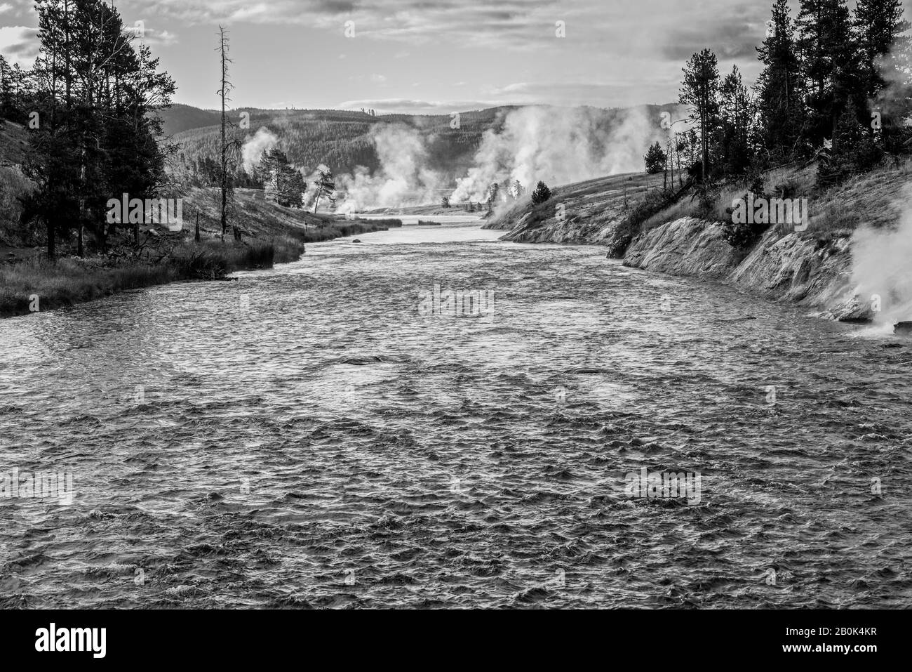 Schnell fließender Fluss in Richtung Geysire, der Dampf und bewaldete Hügel entlüftet. Stockfoto