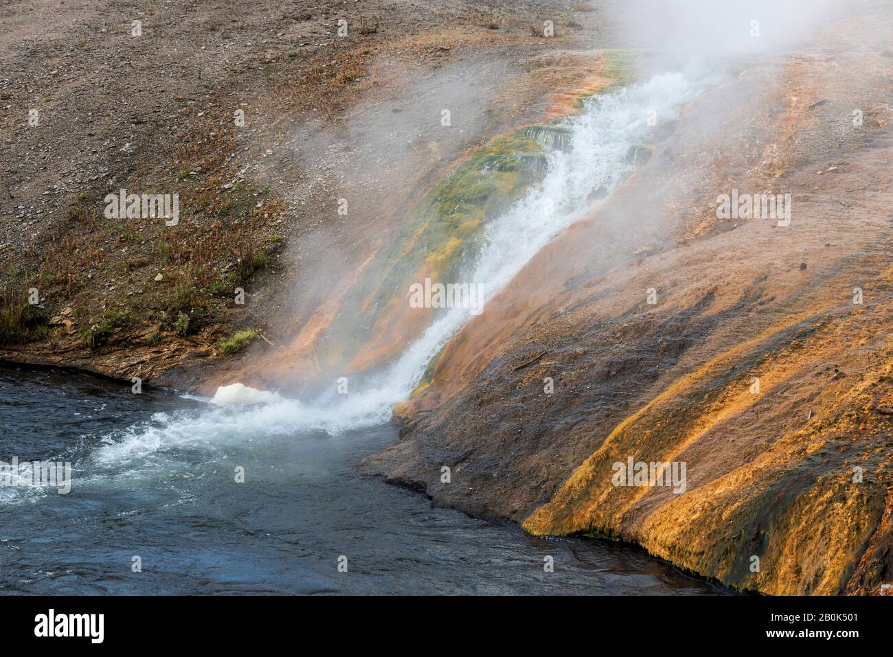 Heißes, dampfendes Wasser fließt an einem grünen, orangefarbenen und braunen Hang entlang in einem kalten, blauen Fluss. Stockfoto