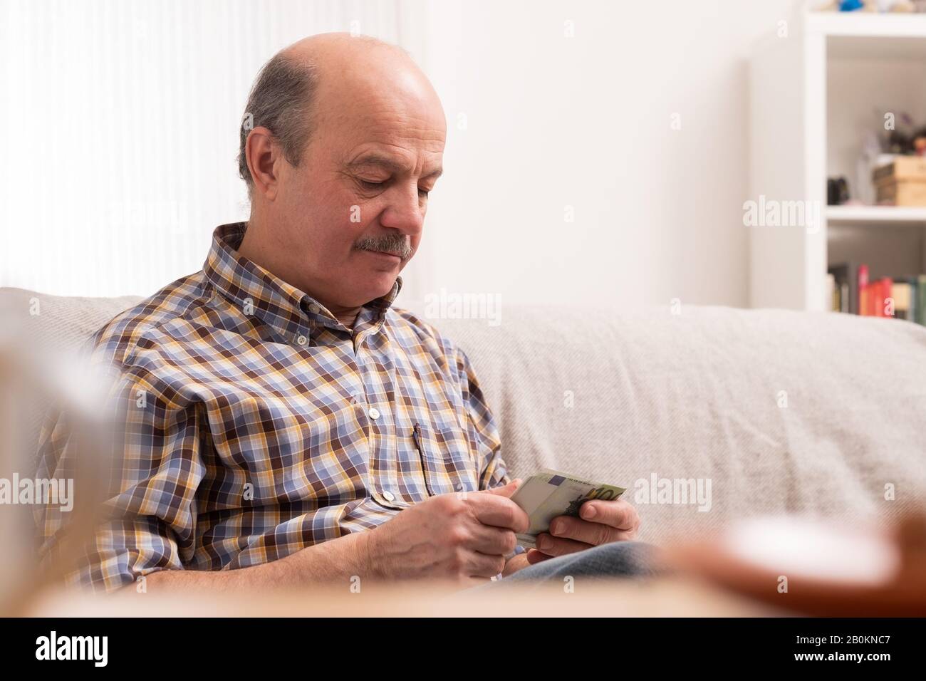 Der ältere Glatze mit Schnurrbart beschäftigt sich mit dem zählen von Geld und Rechnungen zu Hause und sitzt allein zu Hause. Stockfoto