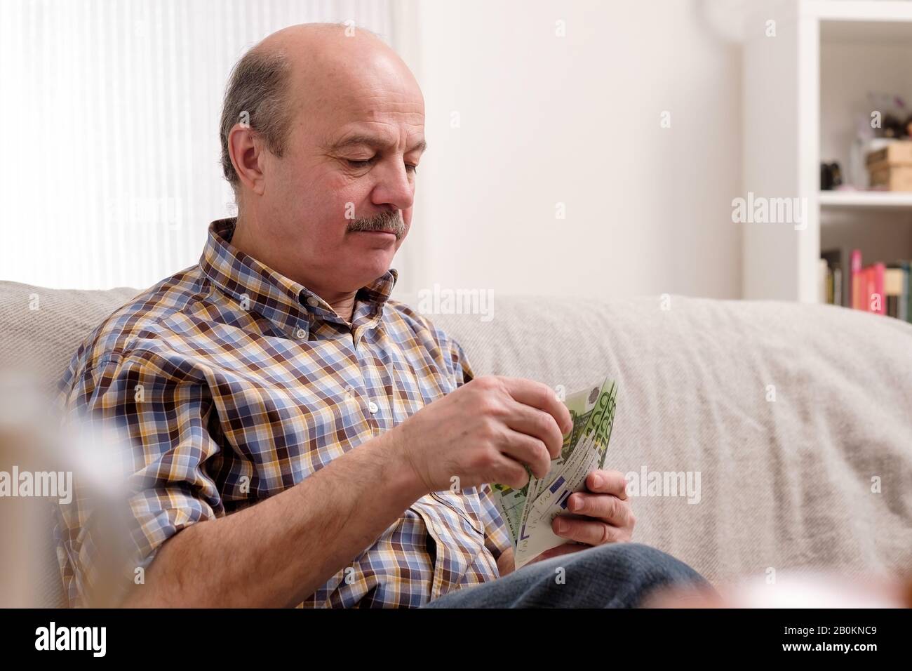 Der ältere Glatze mit Schnurrbart beschäftigt sich mit dem zählen von Geld und Rechnungen zu Hause und sitzt allein zu Hause. Stockfoto