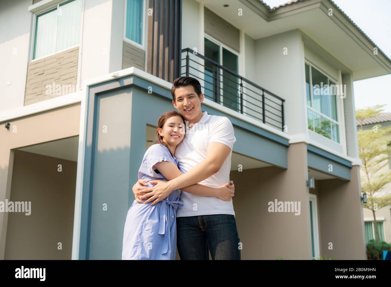 Porträt des jungen asiatischen Paares, das zusammen steht und umarmt und vor ihrem neuen Haus glücklich aussieht, um neues Leben zu beginnen. Familie, Alter, Zuhause, echte Esta Stockfoto